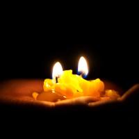 A brown hand holding a yellow candle in the darkness as the candle burns down.